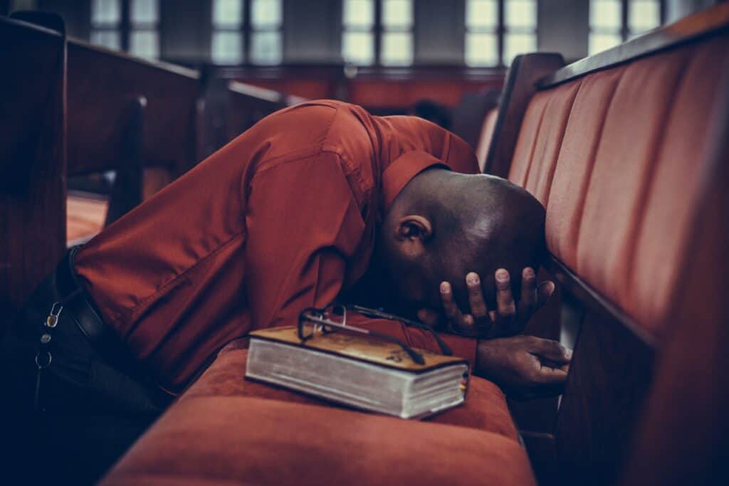 Black man praying on his knees with head in hand